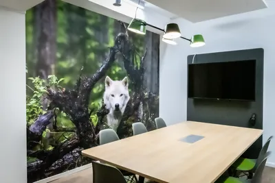 Ein Raum mit einem Holztisch, um den 6 Stühle stehen. Sie stehen vor einer Wand mit einem Motiv, das einen weißen Wolf im Wald zeigt